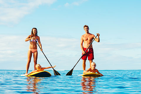 A family enjoying their stand up paddleboard rental from Adventure Water Sports in Fort Myers Beach, Florida, which is available for free at Xplorie participating properties.