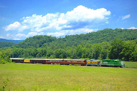 A diesel train from Great Smoky Mountains Railroad travels across a beautiful landscape in Bryson City, North Carolina, which guests can enjoy for free when staying at an Xplorie participating property.