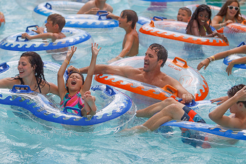 A little girl throws her arms up in delight while in the wave pool with her family at Schlitterbahn Waterpark in Galveston, texas, where guests staying at Xplorie participating properties can enjoy a free admission.